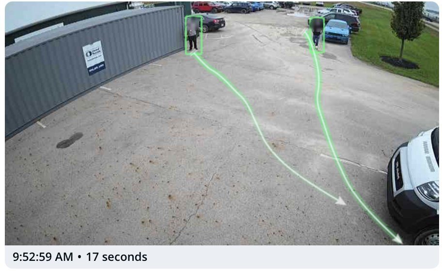 Camera view of a parking lot with green motion trails tracing two people's paths